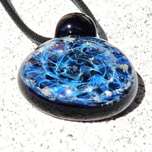 Close-up of black glass pendant containing pet ashes on a black adjustable cord. Made to order by DragonFire Glass