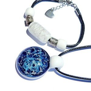 May include: A bracelet and a pendant necklace featuring black cords. The bracelet has white beads, silver-toned spacers, and a heart charm. The pendant is a circular glass piece with a deep blue and swirling light blue pattern with silver flecks.