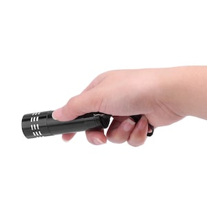 May include: A black flashlight with a silver ring around the head and a black wrist strap.