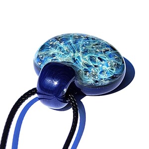 A blue glass memorial pendant with a swirling design in shades of blue infused with ashes. The pendant is attached to a black cord. The urn pendant has a rounded shape with a dark blue, rounded attachment.