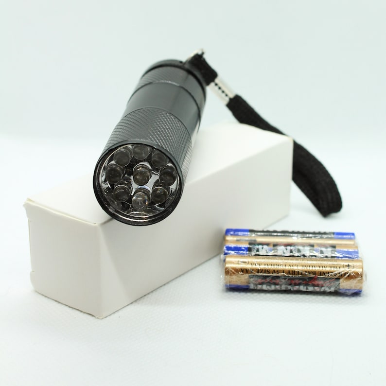 May include: A black flashlight with a wrist strap and a clear lens with multiple LED lights. The flashlight is packaged in a white box with three batteries.