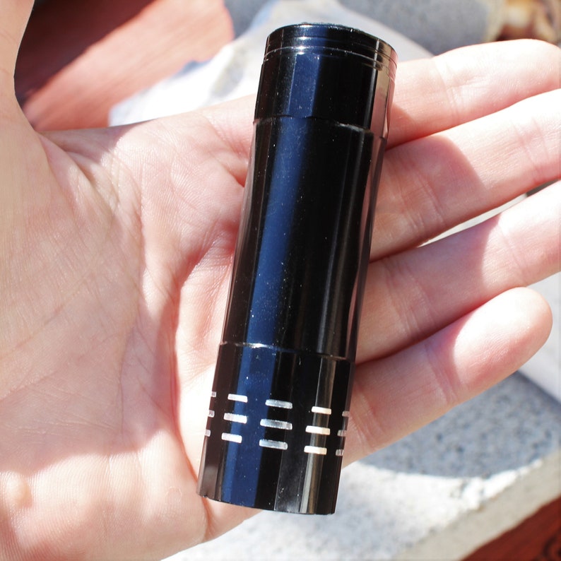 May include: A black flashlight with a silver band around the middle. The flashlight is about 6 inches long.
