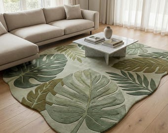 May include: A large, leaf-shaped area rug with a light green background and various shades of green tropical leaves. The rug is placed on a hardwood floor, with a beige sofa and marble coffee table in the background.