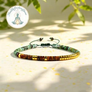 May include: A beaded bracelet featuring a mix of turquoise, brown, and gold-colored beads. The bracelet is strung on a green cord and has an adjustable closure. The text "find your spark" is visible.