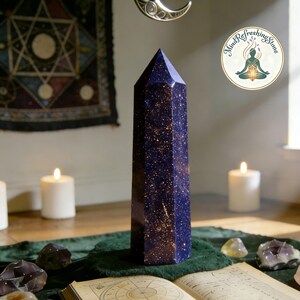 May include: A tall, six-sided blue goldstone crystal tower with a polished finish and embedded copper-colored glitter particles. The stone features a deep navy blue base color with reflective metallic flecks throughout its vertical, pointed structure.