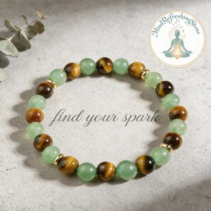May include: A beaded bracelet featuring alternating green and brown tiger eye stones, with gold-colored spacers. The bracelet has the text "find your spark" in a cursive font. A circular logo with a meditating figure is in the upper right corner.