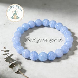 Könnte beinhalten: Ein hellblaues Perlenarmband mit dem Text "find your spark". Das Armband besteht aus runden, polierten Steinen. Das Bild enthält auch ein Logo und einen Zweig mit Grün.