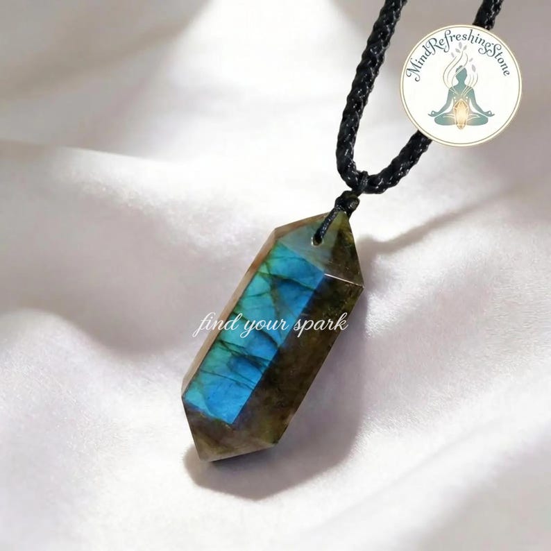 May include: A labradorite crystal pendant with a black cord. The crystal is a hexagonal shape with blue and green iridescent flashes. The text "find your spark" is on the crystal. A circular logo with the text "Mind Refreshing Stone" is in the upper right corner.