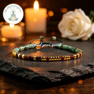 Puede incluir: Una pulsera de cuentas con cuentas turquesas, marrones y doradas. La pulsera está sobre una superficie oscura y texturizada. El texto "find your spark" es visible en la imagen. El fondo incluye velas y una rosa blanca.