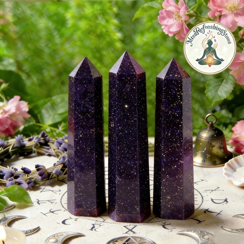 May include: Three dark purple, hexagonal crystal towers with a glittery, gold-flecked appearance. Each stone features a pointed, faceted top and a smooth, polished surface. The crystals stand upright, displaying a deep, starry, midnight-blue hue.