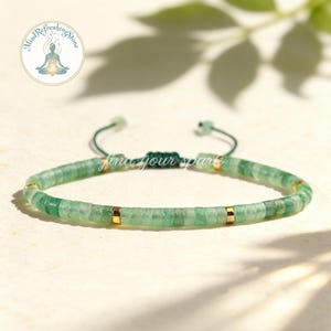 May include: A green beaded bracelet with gold accents. The bracelet is made of small, square-cut green stones strung together on a dark green cord. The bracelet has gold-colored spacers and the text "find your spark".