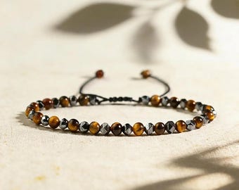 May include: A beaded bracelet featuring alternating round tiger's eye stones and faceted dark metallic hematite beads. The bracelet includes a black adjustable cord closure with two small beads at the ends of the pull strings for a secure fit.
