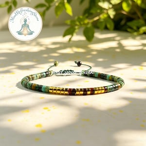 May include: A beaded bracelet featuring a mix of turquoise, brown, and gold-colored beads. The bracelet has a sliding knot closure and is displayed on a light-colored surface. The text "Mind Refreshing Stone" and "goldnourishpark" are visible.