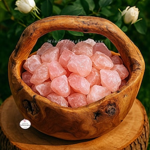May include: A wooden basket filled with raw, light pink rose quartz stones. The basket has a curved handle and sits on a wooden surface. The background features green foliage and white flowers. The text "Mind refreshing stone" is visible.