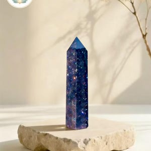 May include: A dark blue, six-sided crystal point featuring a galaxy-like pattern with shimmering flecks of purple, pink, and white. The text MindRefreshingStone and Find Your Spark is printed at the bottom, with a logo in the top left corner.