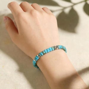 May include: A beaded bracelet featuring small, round, turquoise-colored stones with natural brown veining, interspersed with polished silver-toned metal spacer beads. The bracelet is strung on an elastic cord, creating a flexible, circular band.