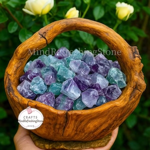 May include: A wooden basket filled with raw fluorite crystals in shades of purple, blue, and green. The basket has a handle and is held by a person. The text "MindRefreshingStone" and "Crafts MindRefreshingStone 2025" are visible.
