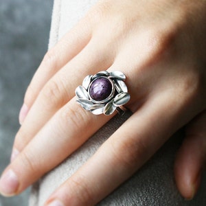 May include: A silver ring featuring a purple gemstone set within a floral design.