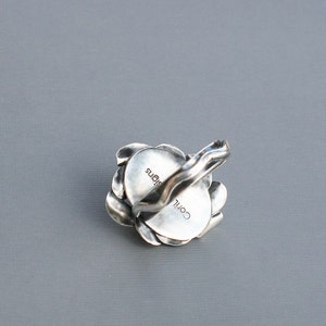 Peut inclure: Une bague en argent avec un motif floral. La bague est grav&eacute;e des mots "COIL" et "SIGNS".