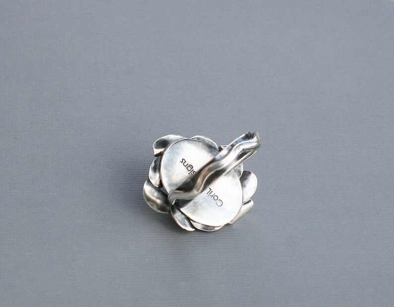 Peut inclure: Une bague en argent avec un motif floral. La bague est grav&eacute;e des mots "COIL" et "SIGNS".