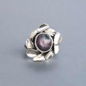 Peut inclure: Une bague en argent avec une grande pierre pr&eacute;cieuse ronde, violette et verte, sertie dans un motif en forme de fleur.