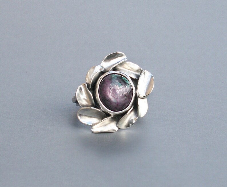 Peut inclure: Une bague en argent avec une grande pierre pr&eacute;cieuse ronde, violette et verte, sertie dans un motif en forme de fleur.