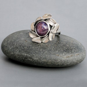 Peut inclure: Une bague en argent avec une pierre pr&eacute;cieuse cabochon violette et bleue sertie dans un motif floral.