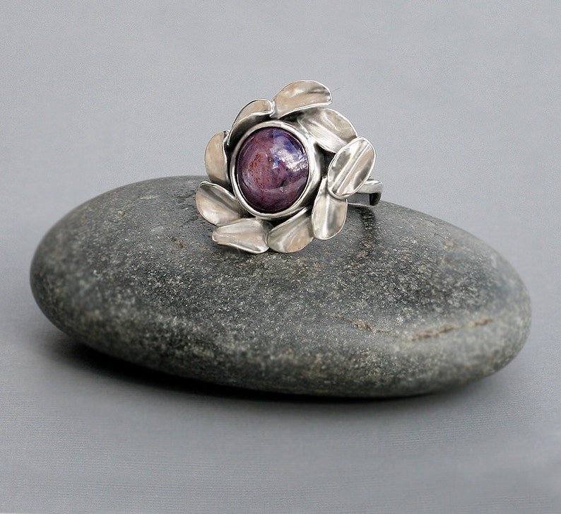Peut inclure: Une bague en argent avec une pierre pr&eacute;cieuse cabochon violette et bleue sertie dans un motif floral.