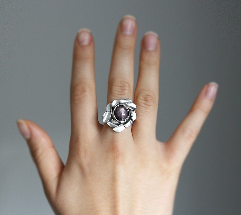 Peut inclure: Une bague en argent avec une pierre pr&eacute;cieuse violette sertie dans un motif en forme de fleur.