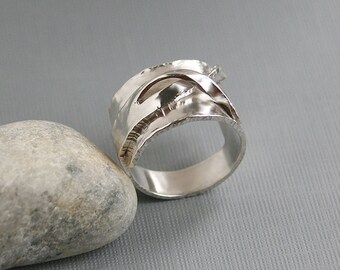 May include: A silver ring with a textured, organic design. The ring is wide and has a smooth, polished interior.