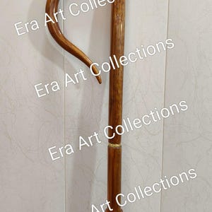 May include: A wooden walking cane with a curved handle. The cane is a rich brown color with a polished finish. The handle has a smooth, rounded shape, and the shaft is straight with a decorative band near the top. The cane is a classic accessory.