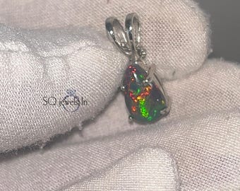 May include: A teardrop-shaped pendant featuring a vibrant opal with flashes of red, green, and yellow. The opal is set in a silver-colored metal frame with a loop for a chain. The pendant is displayed on a white surface.