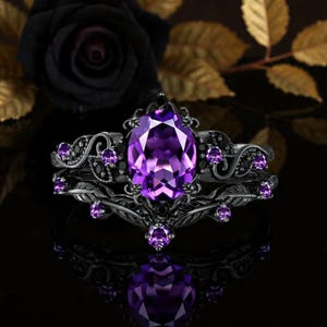 Peut inclure: Un ensemble de bagues noires avec une pierre précieuse ovale violette et de petites pierres violettes. La bague a un design gothique orné avec un motif floral. Le fond présente une rose noire et des feuilles dorées.