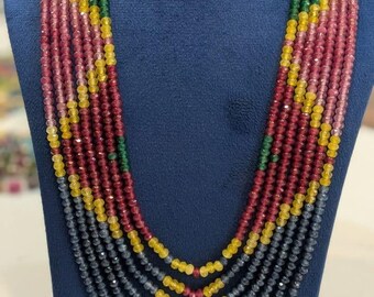 May include: A multi-strand necklace with a variety of colorful beads. The necklace features strands of red, yellow, green, and gray beads. The necklace is displayed on a blue bust.