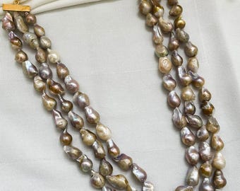 May include: A multi-strand necklace featuring irregularly shaped pearls in shades of brown, gray, and cream. The necklace has gold-colored clasps and a delicate gold chain. The pearls are strung together to create a layered effect.
