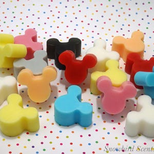 Può includere: Una collezione di cere profumate a forma di Mickey Mouse in vari colori, tra cui giallo, rosa, blu, rosso e nero. Le cere sono disposte su uno sfondo a pois, creando un'estetica giocosa e allegra.