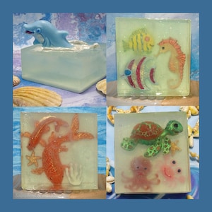 May include: Four square soaps with ocean themes. One soap features a blue dolphin in a clear block. Another has a yellow fish, seahorse, and a red and white fish. The third has orange fish and starfish. The last has a green turtle and pink octopus.