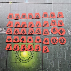 May include: A selection of red and black game pieces featuring diverse symbols. The pieces are laid out on a grey and green patterned surface. The shapes include rectangles, circles, and other geometric forms.