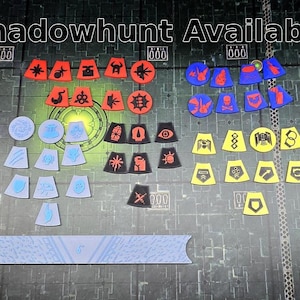 Peut inclure: Ensemble de jetons de jeu de différentes formes et couleurs, notamment rouge, bleu et jaune. Les jetons présentent différents symboles et motifs, avec le texte "Shadowhunt Available" en haut.