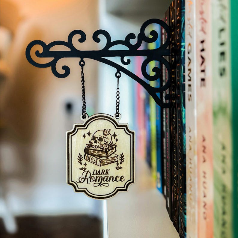 A decorative metal bracket with a hanging sign that reads "Dark Romance" is mounted on a bookshelf filled with various books.