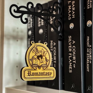 A wooden sign with the word "Romantic" hanging from a black metal bracket, surrounded by books on a shelf.