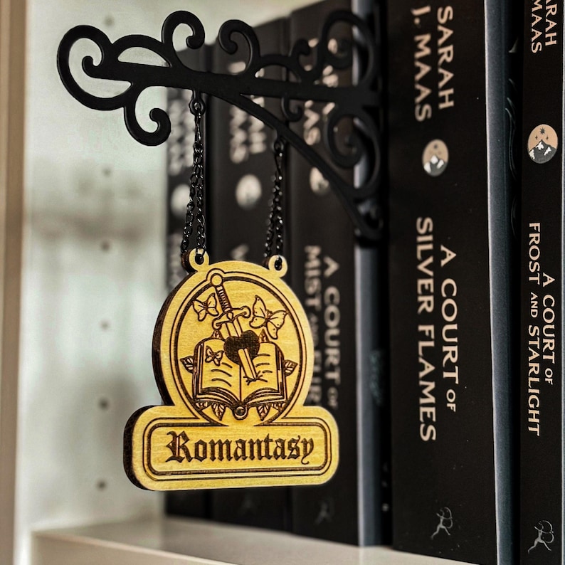 A wooden sign with the word "Romantic" hanging from a black metal bracket, surrounded by books on a shelf.