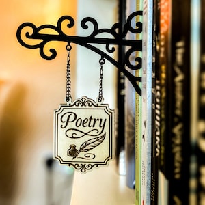 A decorative metal sign with the word "Poetry" hanging from a bookshelf, surrounded by various books.