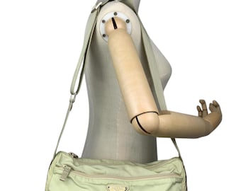 Könnte beinhalten: Hellgrüne Prada Umhängetasche mit rechteckiger Form und langem, verstellbarem Riemen. Die Tasche hat ein Hauptfach mit Reißverschluss und ein kleines, dreieckiges Logo auf der Vorderseite. Die Tasche wird auf einer Schaufensterpuppe präsentiert.
