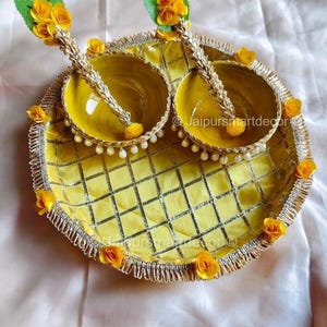 Può includere: Un vassoio da portata giallo decorativo con due ciotole abbinate, ciascuna con un cucchiaio decorativo. Il vassoio e le ciotole sono adornati con fiori gialli e un bordo argentato. Il vassoio ha un motivo a scacchi.