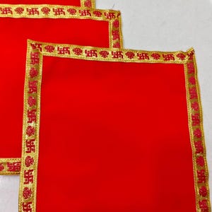 May include: Three red square cloths with gold borders. The borders are decorated with a repeating pattern in red. The cloths are stacked on top of each other, with the top cloth slightly offset, revealing the other cloths.