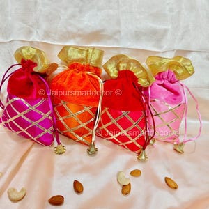 Puede incluir: Cuatro bolsas de terciopelo con cordón en tonos rosa, naranja y rojo, con detalles dorados y un patrón de diamantes. Las bolsas tienen cierres dorados y se muestran con nueces.