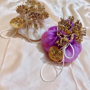 Könnte beinhalten: Zwei dekorative Beutel mit Kordelzug. Einer ist weiß, der andere lila. Beide haben goldene Blumenverzierungen und goldene kreisförmige Akzente. Weiße Kordelzüge sind angebracht. Der Text "Jaipur smart decor" ist sichtbar.