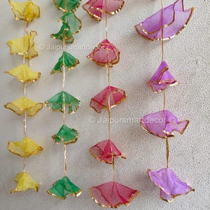 May include: Decorative hanging ornaments in yellow, green, pink, and purple. Each ornament has a delicate, sheer fabric design with gold trim, suspended by a thin gold string. The ornaments are arranged in vertical rows, creating a visually appealing display.