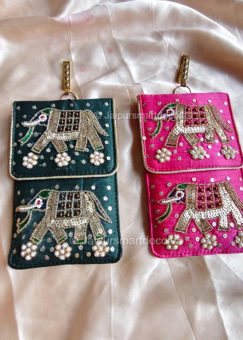 May include: Two decorative phone pouches, one in emerald green and the other in fuchsia. Each pouch features an embroidered elephant design with sequins and beads. They have a rectangular shape with a flap and a gold-colored metal clasp.